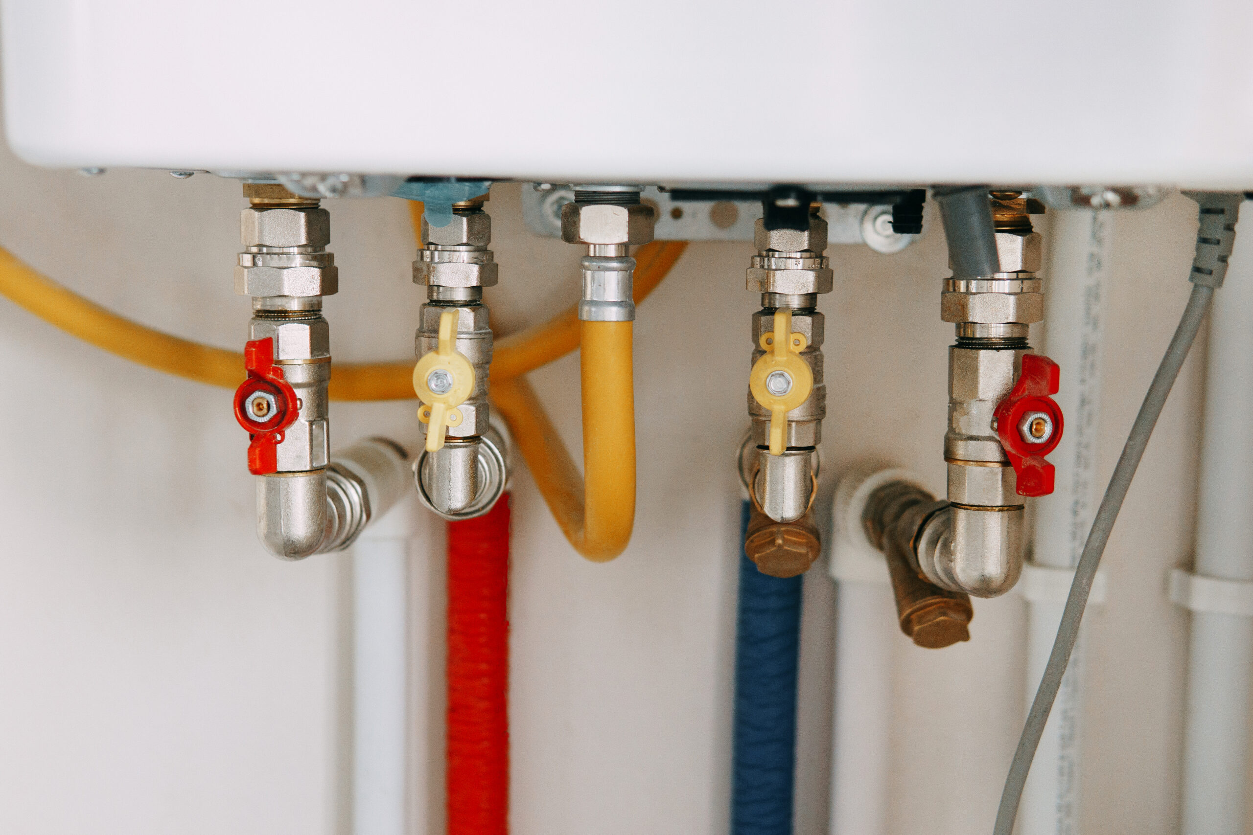 Close-up view of water heater pipes and valves in a utility room, featuring colorful connectors and tubes. Essential components for heating system maintenance and operation. Gas boiler taps.